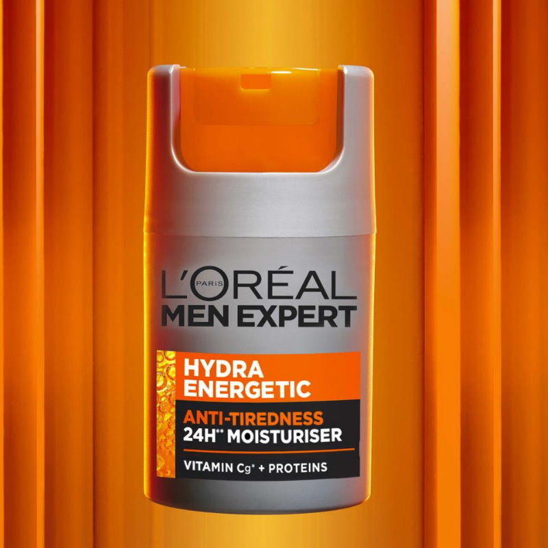 L'Oréal Paris Men Expert Hydra Energetic Anti-Tiredness 24H Moisturiser in a cylindrical pump bottle with a gray body, orange cap, and orange/black label, centered against a vertical orange gradient background.